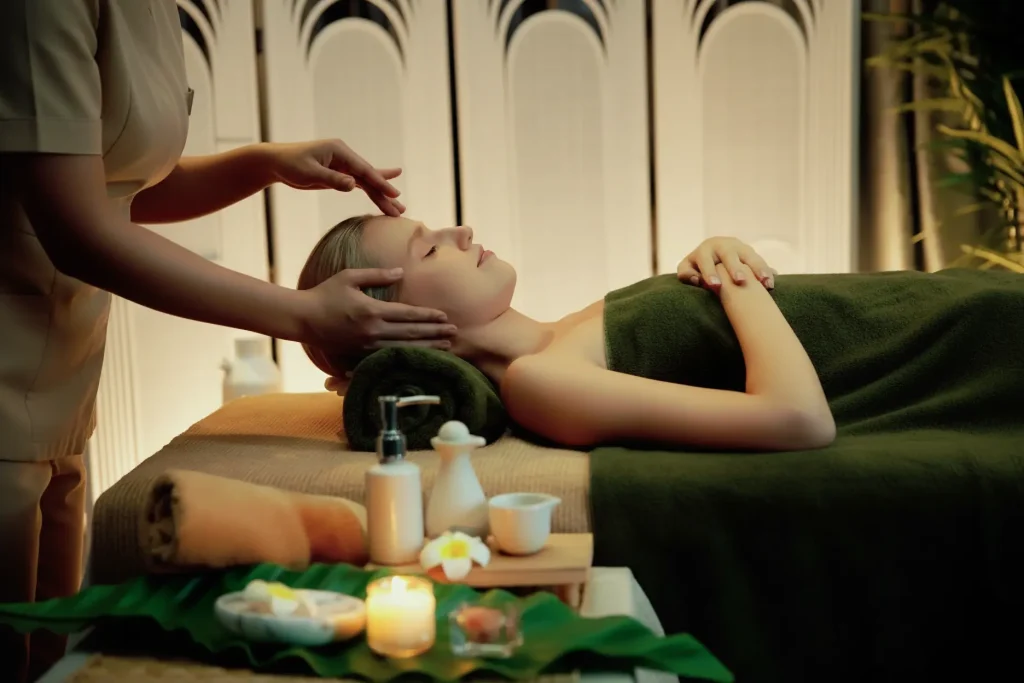 A professional massage therapist in a beige uniform providing a relaxing treatment in a white, dimly lit spa room at Seoyeon Beauty Salon in Al Ain.